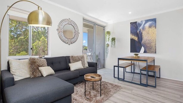 A modern living room with a grey sofa, a round coffee table, and a dining table with benches. - 12 Calming Coral Beach Beautiful 2BRM (Scarborough)