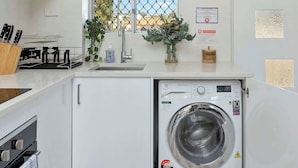 A compact kitchen with a built-in washing machine, a window with a view, and a door with a small window. - 12 Calming Coral Beach Beautiful 2BRM (Scarborough)