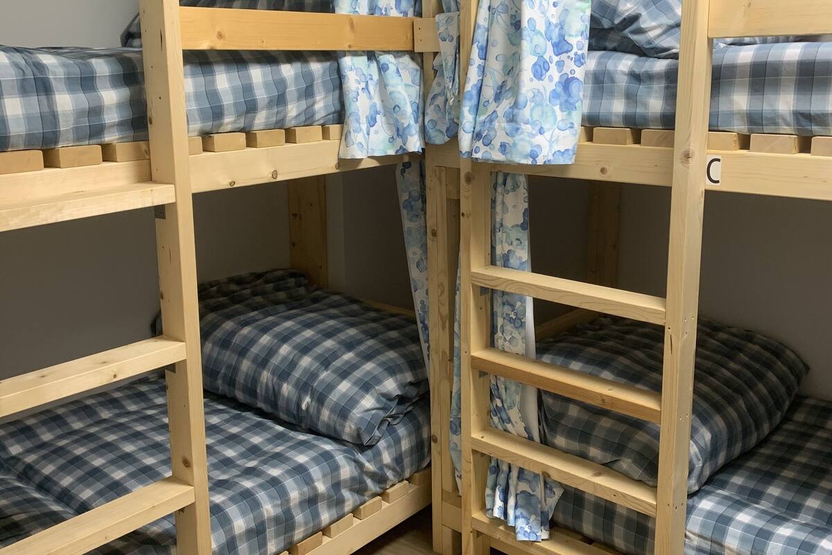 A bunk bed room with wooden frames, plaid bedding, and a curtain with a blue floral pattern.