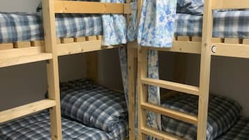A bunk bed room with wooden frames, plaid bedding, and a curtain with a blue floral pattern.