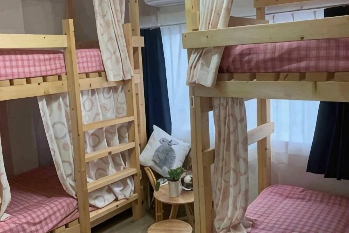 A bunk bed room with a small table and chair, a pillow, and a window with curtains.