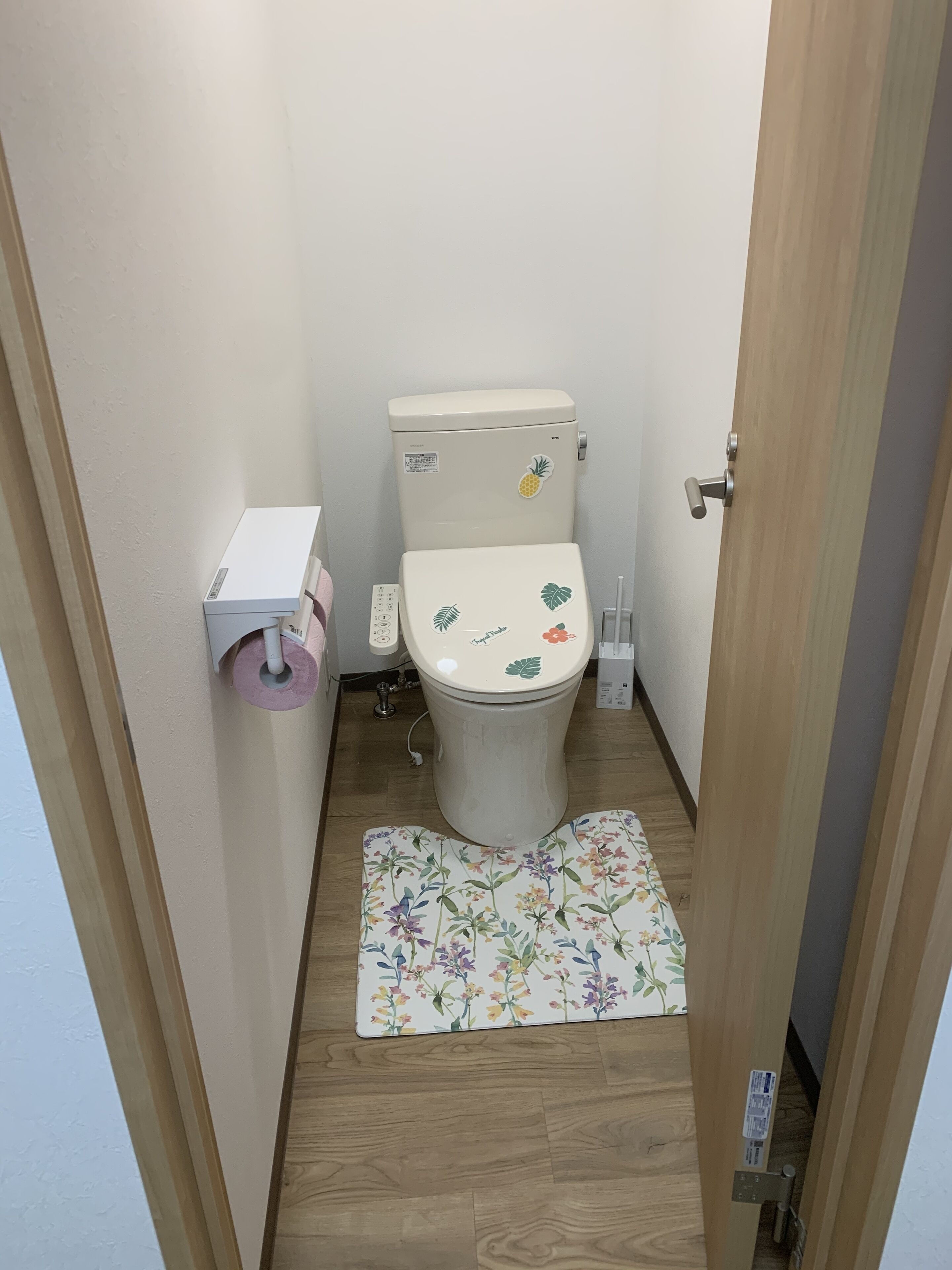 A small bathroom with a toilet, a toilet paper holder, and a wooden floor.