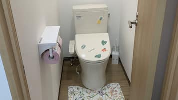 A small bathroom with a toilet, a toilet paper holder, and a wooden floor.