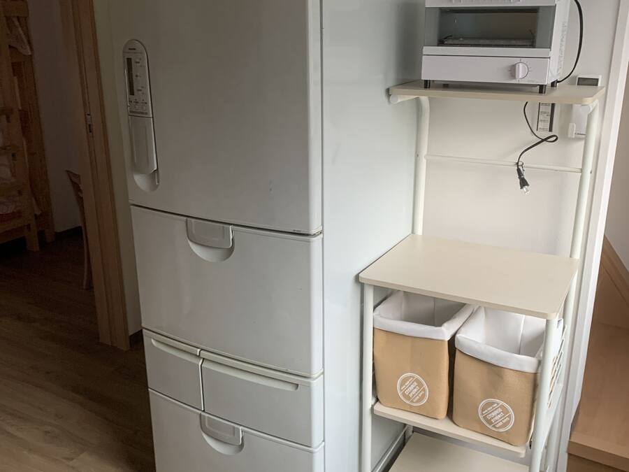 A white refrigerator with a built-in microwave, a small shelf with storage bins, and a wooden door frame.