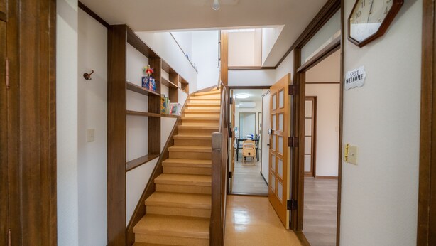 A hallway with a wooden staircase leading to another room. There are wooden doors on either side, a clock on the right wall, and a 'Welcome' sign above the door. - Minpaku Ota Building No.2 (Otaru)