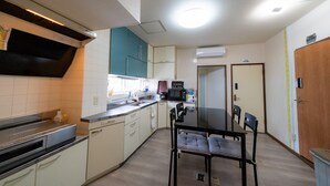 A compact kitchen with a microwave, sink, and a dining area with chairs. - Minpaku Ota Building No.2 (Otaru)