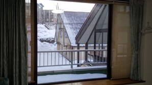 A window with a view of a snowy outdoor area, including a building with a sloped roof and a satellite dish. - Minpaku Ota Building No.2 (Otaru)