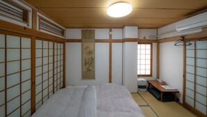A traditional Japanese-style room with tatami flooring, a futon bed, a shoji screen, and a sliding door. - Minpaku Ota Building No.2 (Otaru)