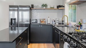 Une cuisine moderne avec des meubles de couleur noire, des appareils électroménagers en acier inoxydable, un four à micro-ondes, une machine à café et une cuisinière à gaz.