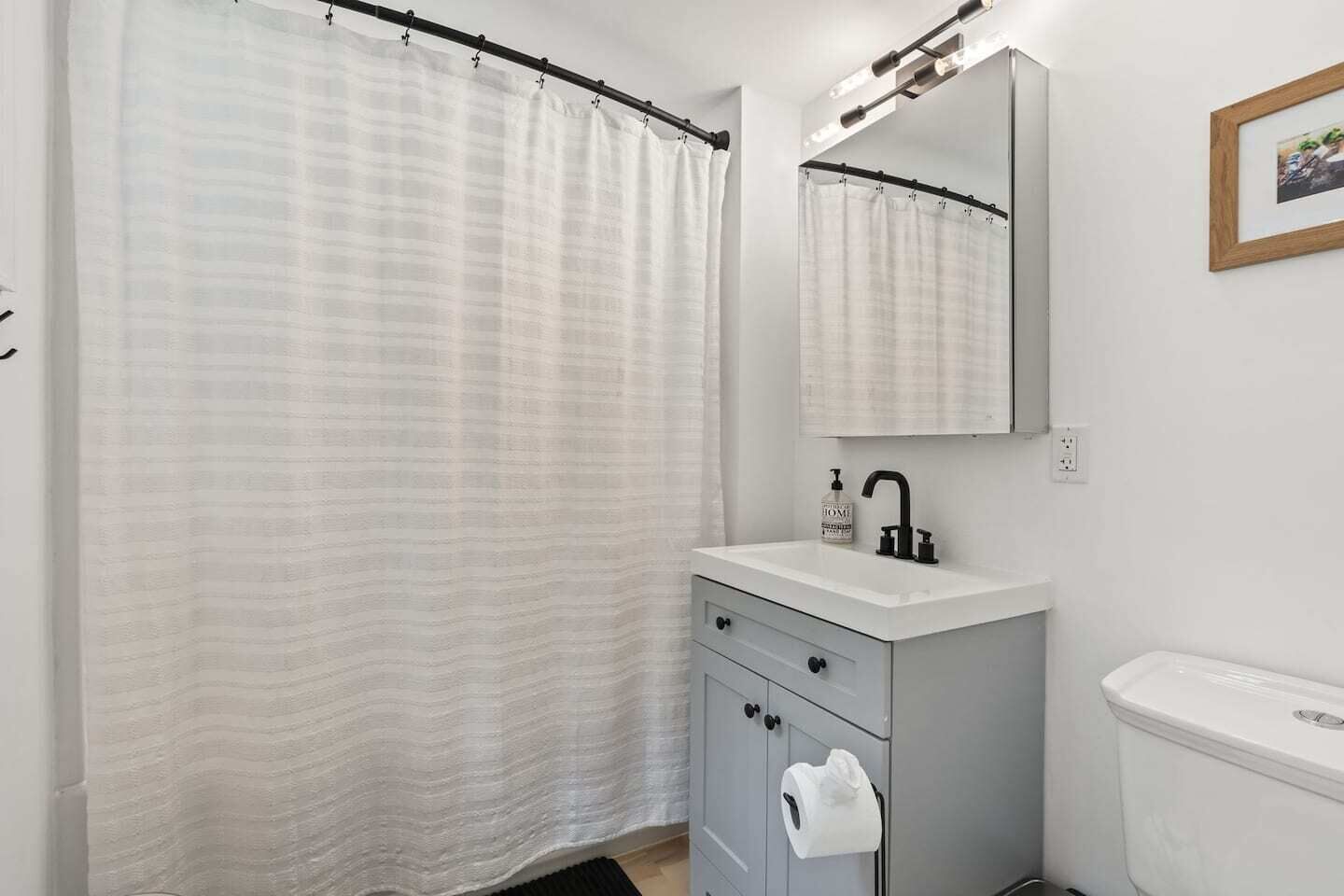 Un baño con cortina de ducha, un lavamanos con espejo y un inodoro.