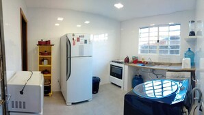 A compact kitchen with a refrigerator, stove, sink, and a window providing natural light. - Comfortable house in Florianópolis |Moçambique Beach (Florianópolis)
