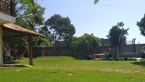 A grassy outdoor area with a wooden structure, a hammock, and a red object. - Comfortable house in Florianópolis |Moçambique Beach (Florianópolis)