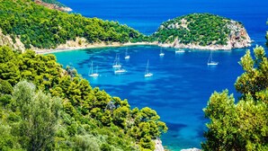 A coastal bay with clear blue waters, surrounded by lush green hills and rocky outcrops. - Sailing between the Sporades Islands (Sciato)