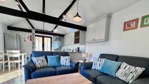 A modern living room with a dark blue sofa set, a wooden coffee table, and a kitchen in the background. - Dog and family friendly barn conversion with fully enclosed garden and hot tub (Dilham)