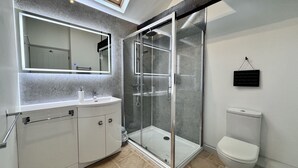 A modern bathroom with a glass-enclosed shower, a white toilet, and a large mirror above the sink. - Dog and family friendly barn conversion with fully enclosed garden and hot tub (Dilham)