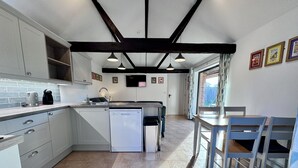 A modern kitchen with a dishwasher, a coffee maker, and a sink. There is a dining area with a table and chairs. - Dog and family friendly barn conversion with fully enclosed garden and hot tub (Dilham)