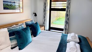 A neatly made bed with blue and white bedding, a framed picture on the wall, and a window with curtains. - Dog and family friendly barn conversion with fully enclosed garden and hot tub (Dilham)