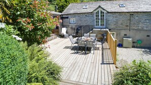 A stone building with a wooden deck, outdoor seating, and a barbecue area. - Stone Barn is a stunning barn in an idyllic hamlet, sleeps 6, games room, + dogs (Lanteglos)