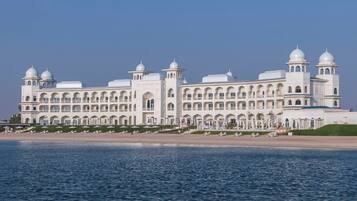 A large, white, multi-story building with arched windows and domed roofs, situated by a body of water.