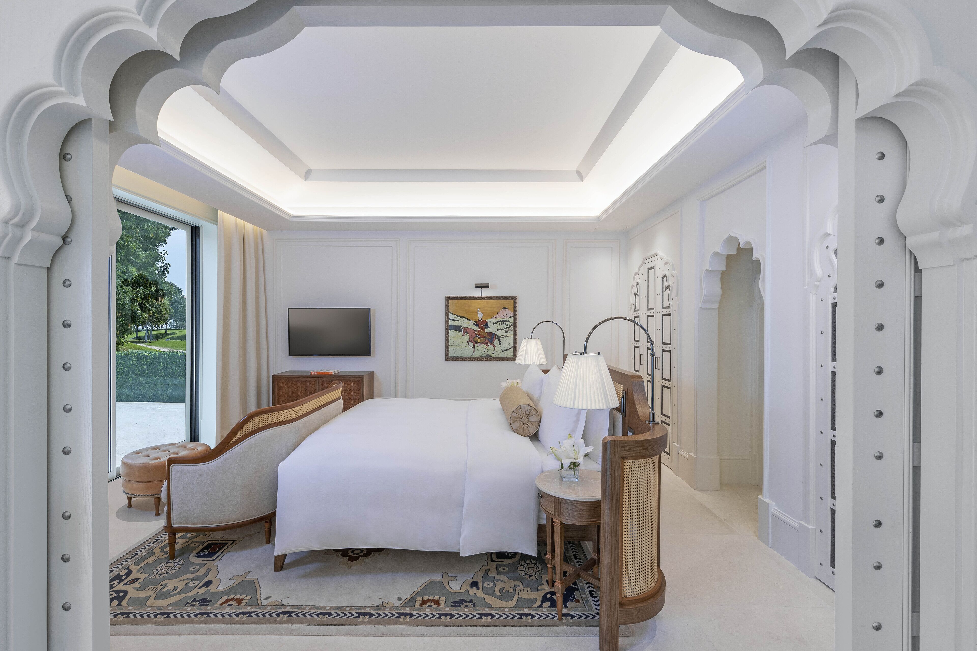 Un dormitorio amplio con una cama grande, un televisor y vistas a un paisaje verde por la ventana.