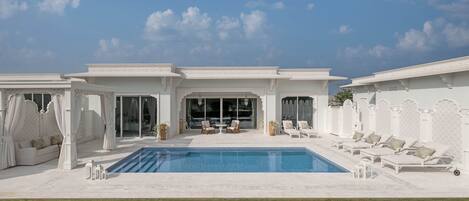 A poolside area with a pool, lounge chairs, and a seating area with a table and chairs.