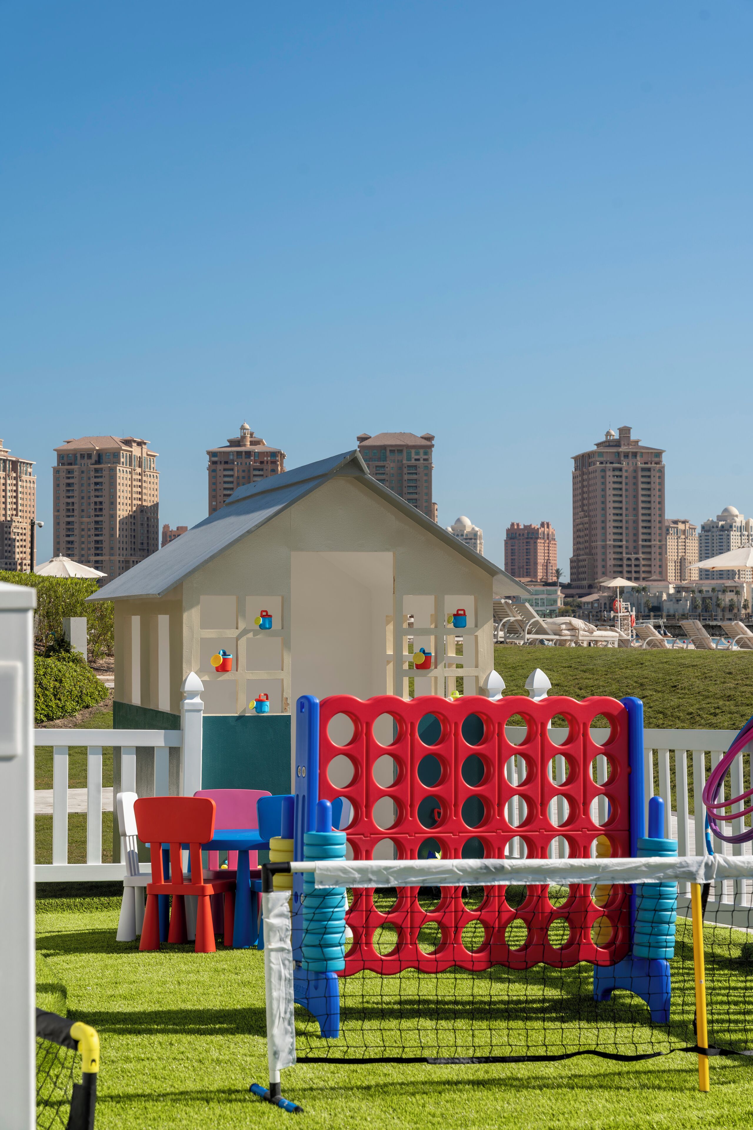 A children's play area with a soccer goal, colorful play structures, and a white fence.