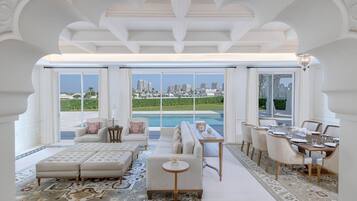 Amplia sala de estar con un sofá grande, una mesa de comedor dispuesta para seis personas y vistas a la ciudad y a la piscina.