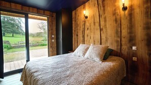 Ein Schlafzimmer mit einem großen Bett, Holzwänden und Gartenblick durch eine Schiebetür.
