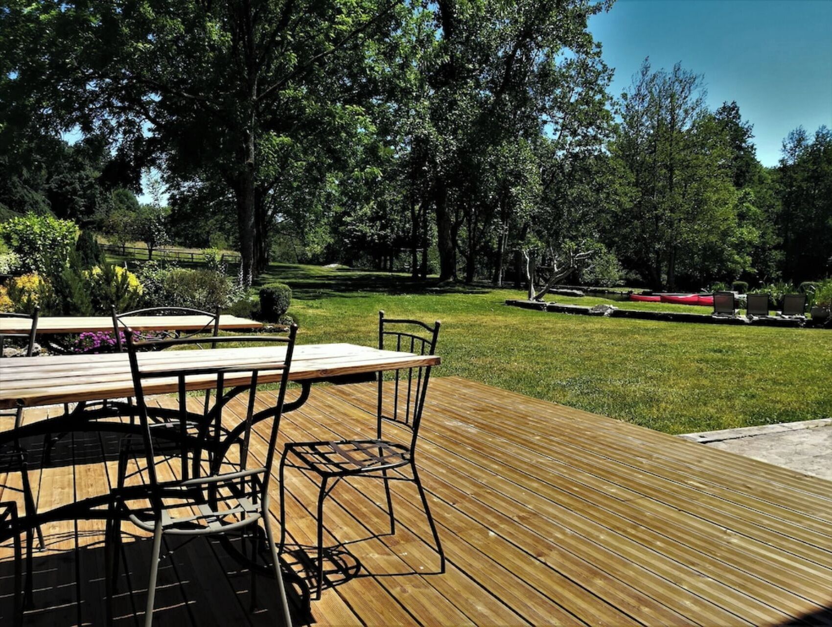 Una terrazza esterna in legno con tavolo e sedie, immersa nel verde e alberi.