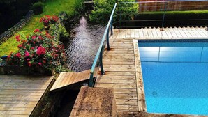 Eine Holzterrasse mit Pool, umgeben von einem Garten mit Blumen und einem kleinen Wasserspiel.