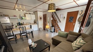 Un salon moderne avec un canapé, une table à manger et des chaises. Il y a également un coin cuisine avec des placards et un réfrigérateur. Un escalier mène à un autre niveau.