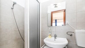 Un baño con ducha, lavamanos, espejo y toallero.