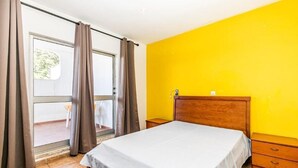 Un dormitorio con cama, una mesita de noche de madera y un ventanal corredero que da a un espacio exterior.