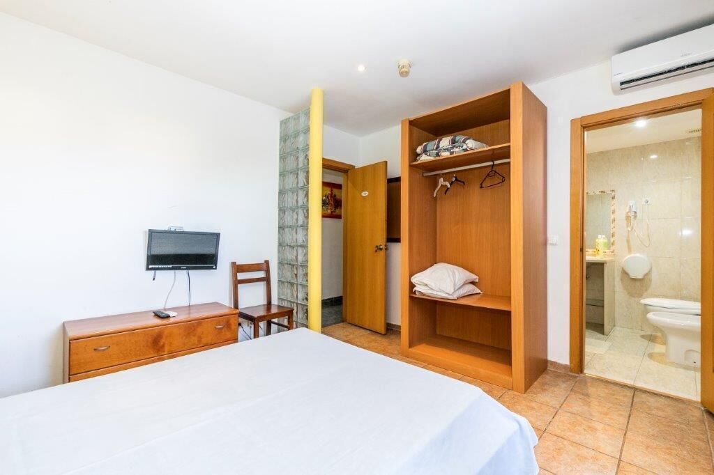 A bedroom with a bed, a TV, a wooden wardrobe, and a bathroom visible through an open door.