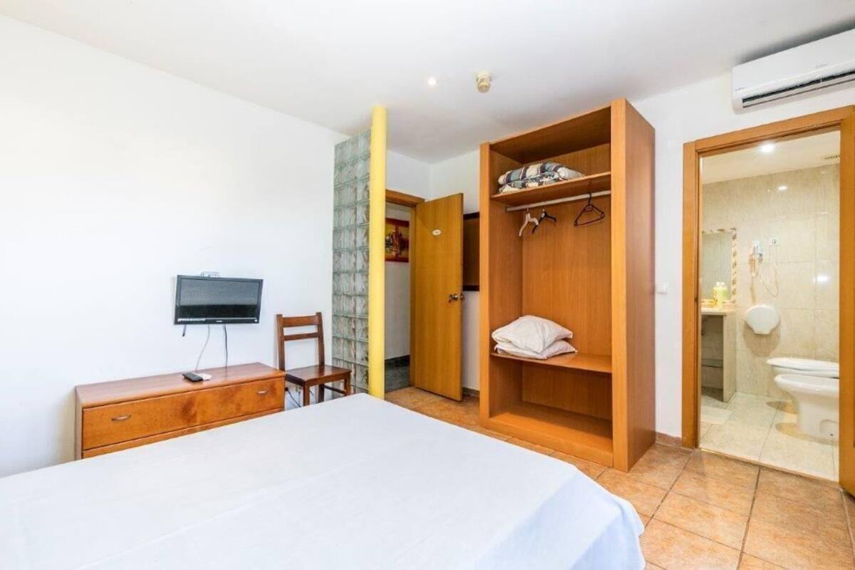 A bedroom with a bed, a TV, a wooden wardrobe, and a bathroom visible through an open door.