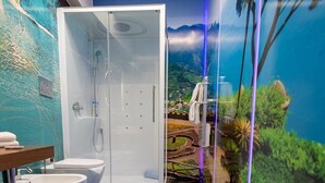 Casa de banho com cabine de duche em vidro, duas lavatórios e um mural com paisagem.