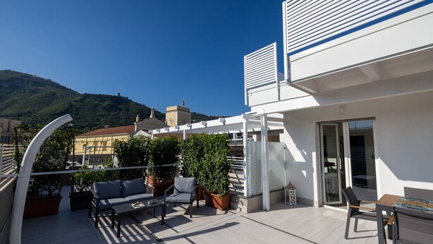 Terraço no telhado com área de estar externa, plantas em vasos e vista dos edifícios e colinas ao redor.