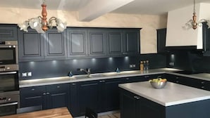A modern kitchen with dark cabinetry, stainless steel appliances, and a wooden dining table. - L'Antidote, estate with heated indoor pool 1h30 from Paris (Coulours)