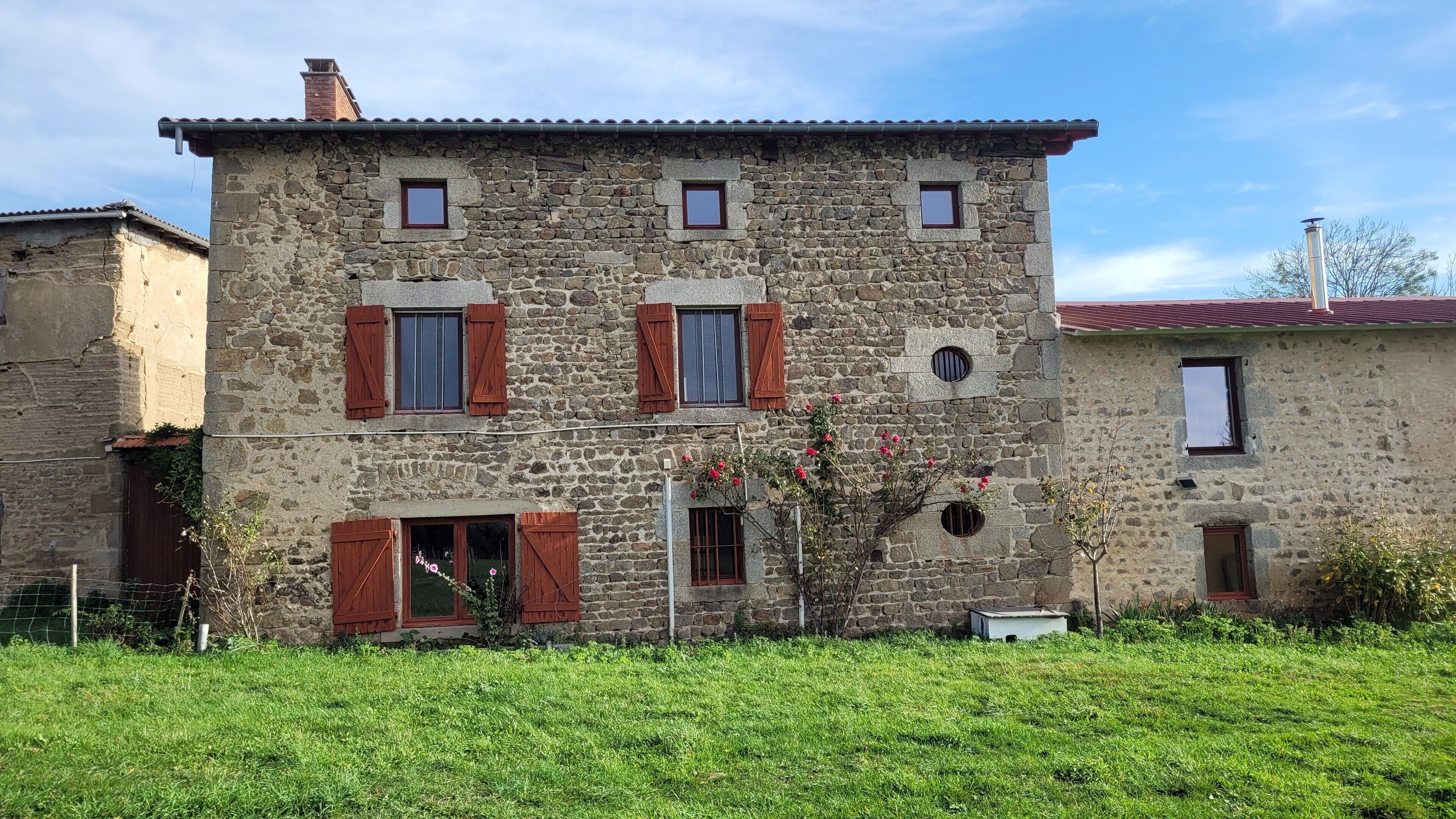 A stone building with multiple windows and shutters, surrounded by a grassy area.