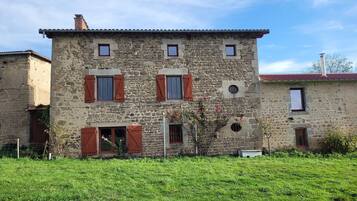 A stone building with multiple windows and shutters, surrounded by a grassy area.