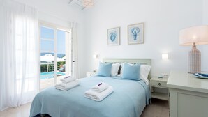 A bedroom with a bed, two bedside tables, a nightstand, a lamp, and a view of the outdoors. - Thea Lofou House (Corfu)