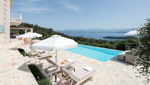 A pool area with lounge chairs and umbrellas, overlooking a scenic view of the sea and mountains. - Thea Lofou House (Corfu)