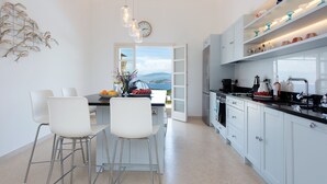 A modern kitchen with white cabinets, a black countertop, and a view of the mountains through an open door. - Thea Lofou House (Corfu)