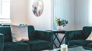 Een moderne woonkamer met een glazen salontafel, twee groene banken, een ronde spiegel en een potplant.