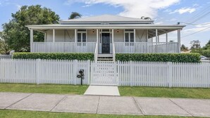 Een gelijkvloers huis met een witte schutting, een veranda en een kleine voortuin.