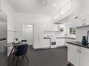 A modern kitchen with white cabinets, a dining area with a round table and chairs, and a built-in oven. - Urban Getaway Queenslander close to Willowbank! (Newtown)