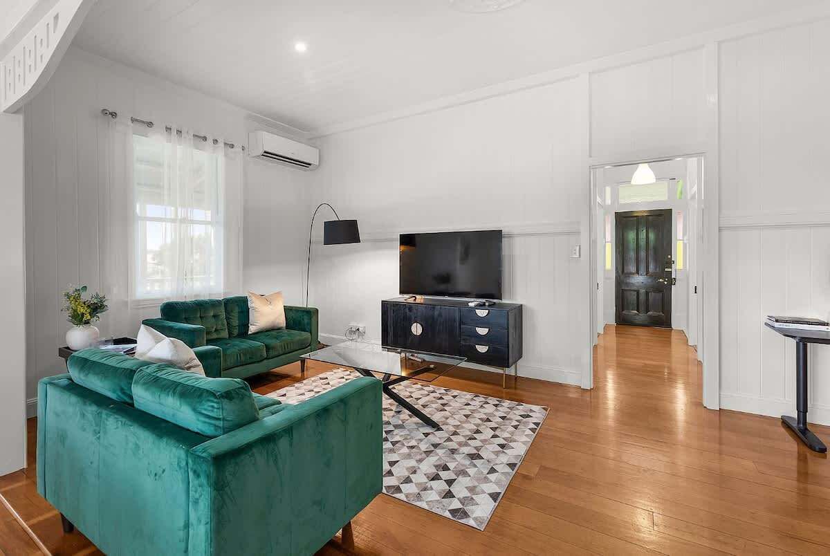 A living room with a green sofa, a flat-screen TV, a black cabinet, and a patterned rug.