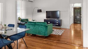 Een moderne woonkamer met een groene bank, een flatscreen televisie, een eettafel met stoelen en een houten vloer.