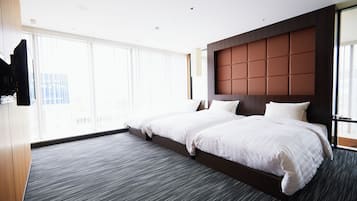 A hotel room with a large bed, a flat-screen TV mounted on the wall, and a large window providing a city view.