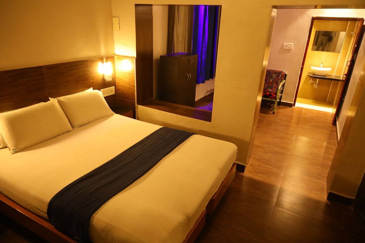 A hotel room with a bed, bedside lamps, a wardrobe, a bathroom with a sink, and a mirror.